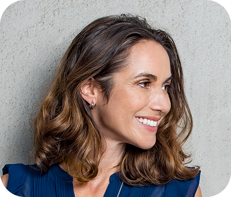 closeup of a woman in a blue top smiling against a concrete wall