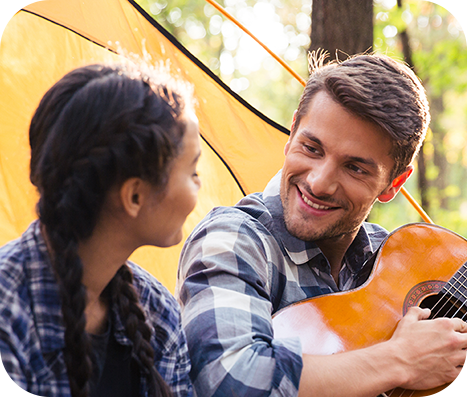 man playing an acoustic guitar for his wife while camping