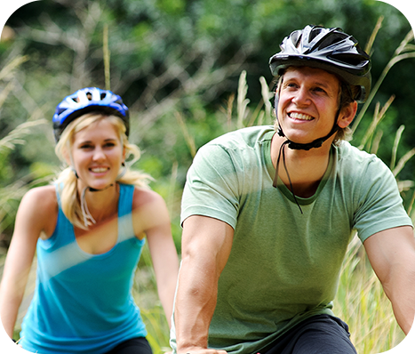 helmeted couple biking in a park with tall grass
