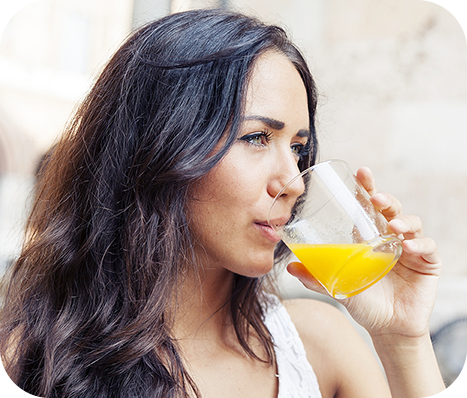 woman in a white tank top drinking orange juice